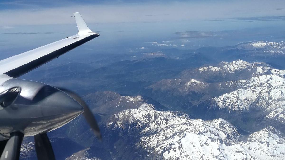 Wingtip and four-blade propeller of a Beechcraft 1900D above snow-covered mountains.
