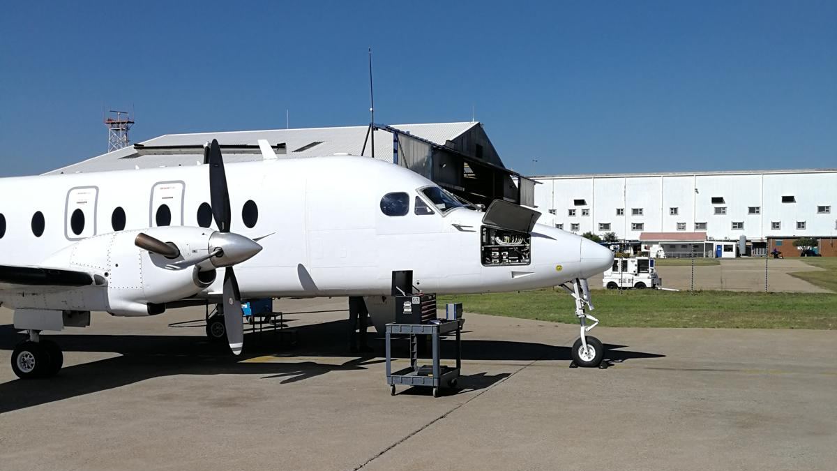 A white Beechcraft 1900D on a ramp with its right engine cowl open.