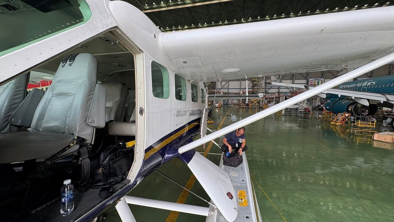 The Cessna Caravan on amphibious floats in a maintenance hangar at Noi Bai International Airport, Hanoi, with a Vietnam Airlines aircraft in the background.