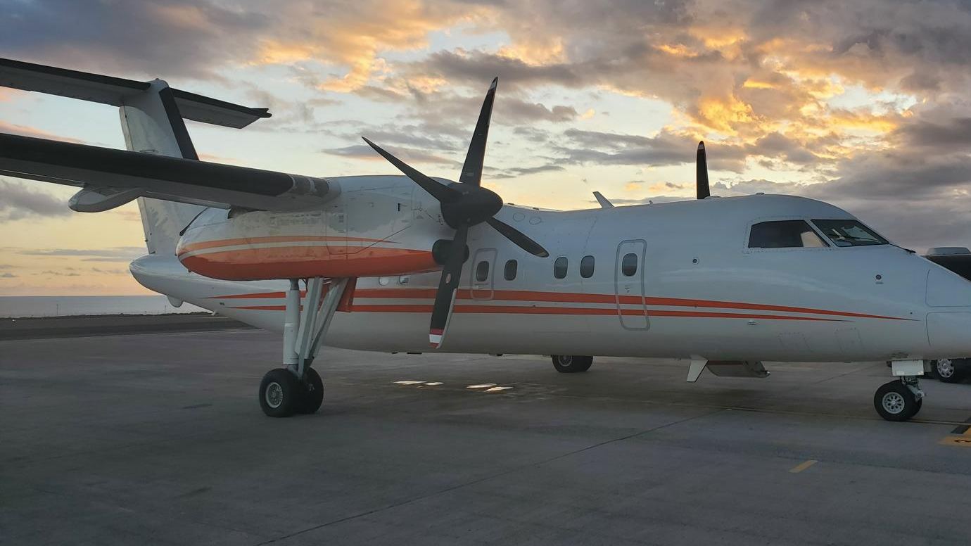 A Dash 8 on a concrete apron under an orange sunset sky.