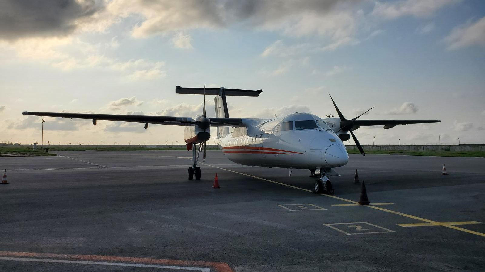 A white Dash 8 with orange stripes parked on an apron at dusk.