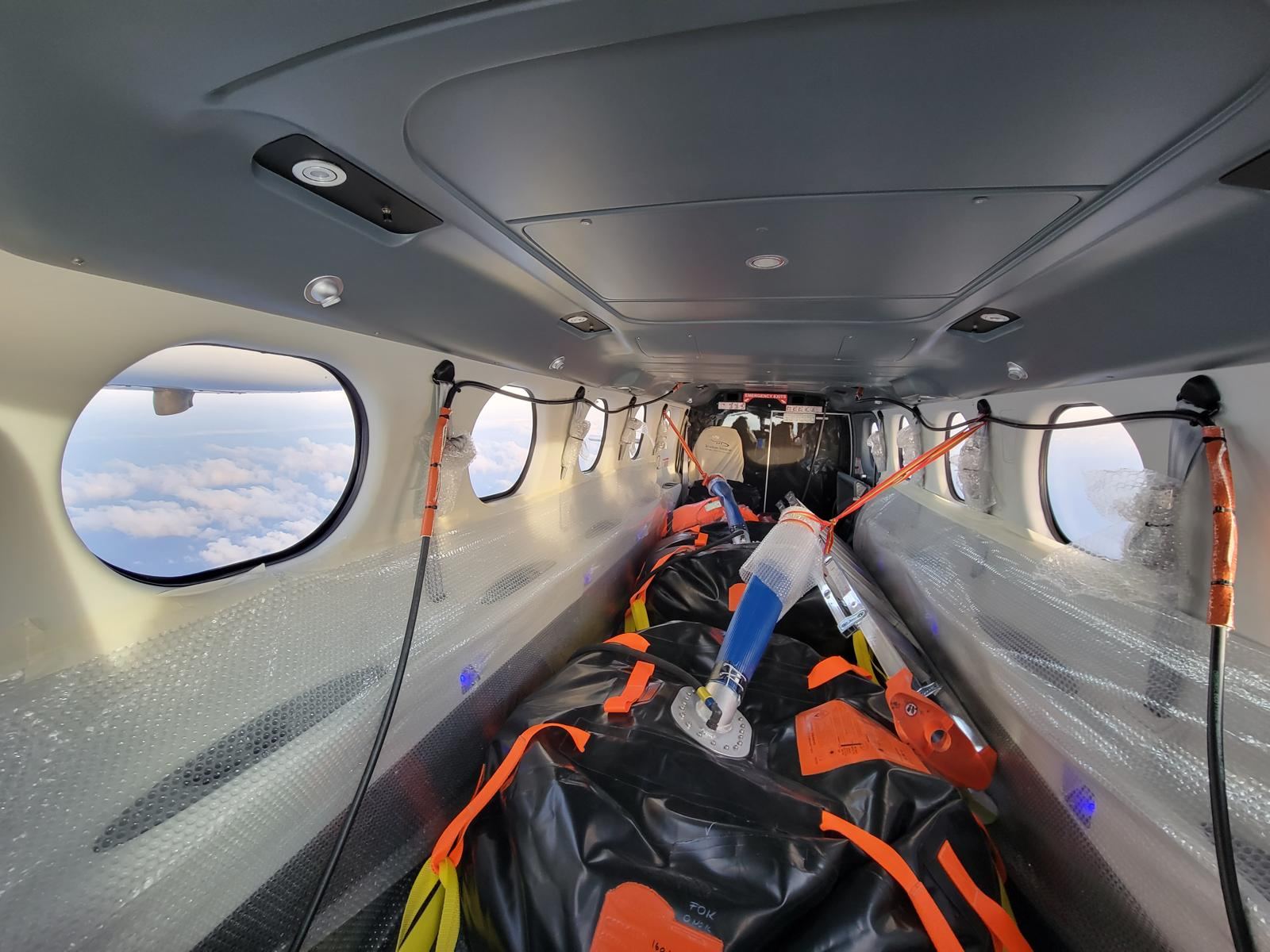The cabin of a Tecnam P2012 with a large black ferry fuel tank strapped along the floor.