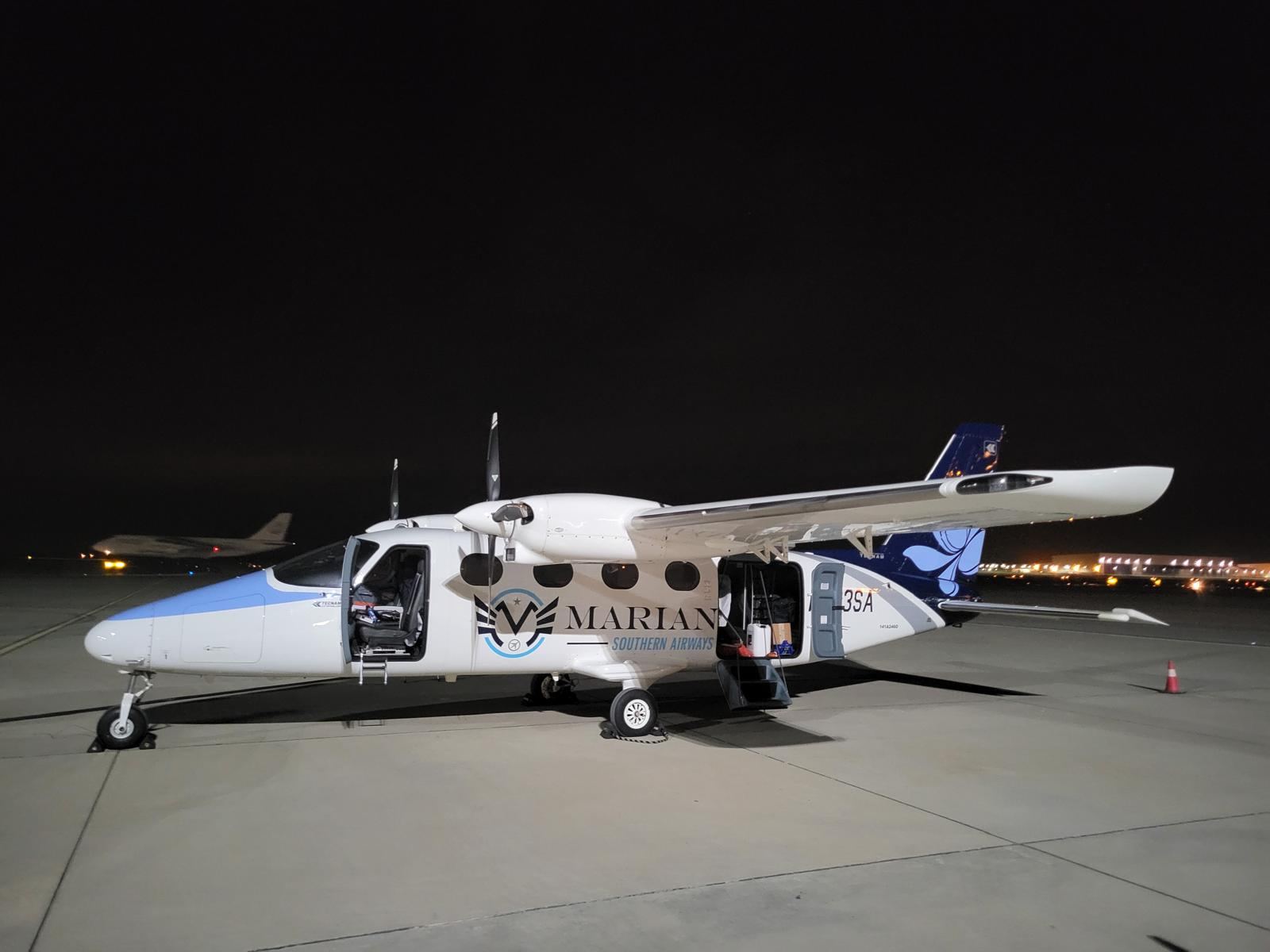 A Tecnam P2012 on a ramp at night with its cabin and baggage doors open.