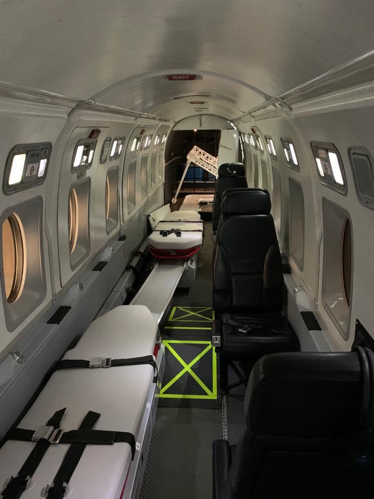 Air ambulance cabin with two stretchers one behind the other on the left side, a floor rail between them, and crew seats on the right.