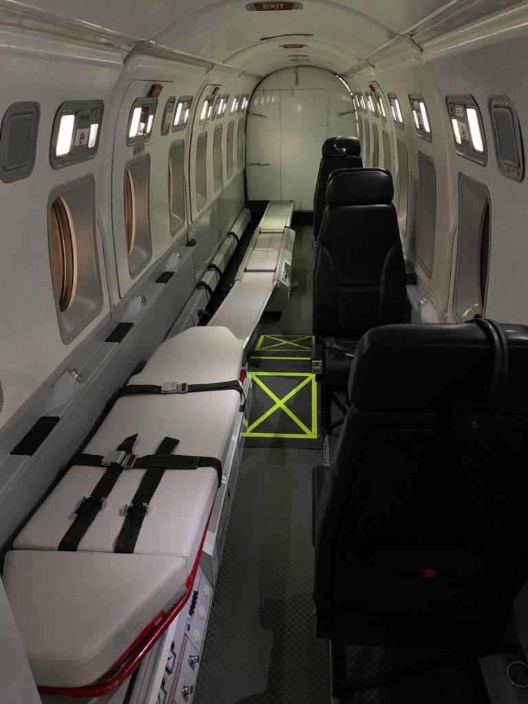 A stretcher on a raised base beside a floor rail, with a row of black crew seats opposite.