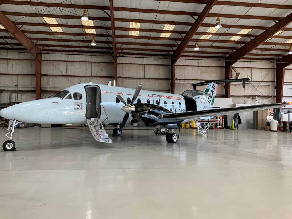 A pale blue Beechcraft 1900D air ambulance with MEDI titles and a star of life, in a hangar with its airstair down.