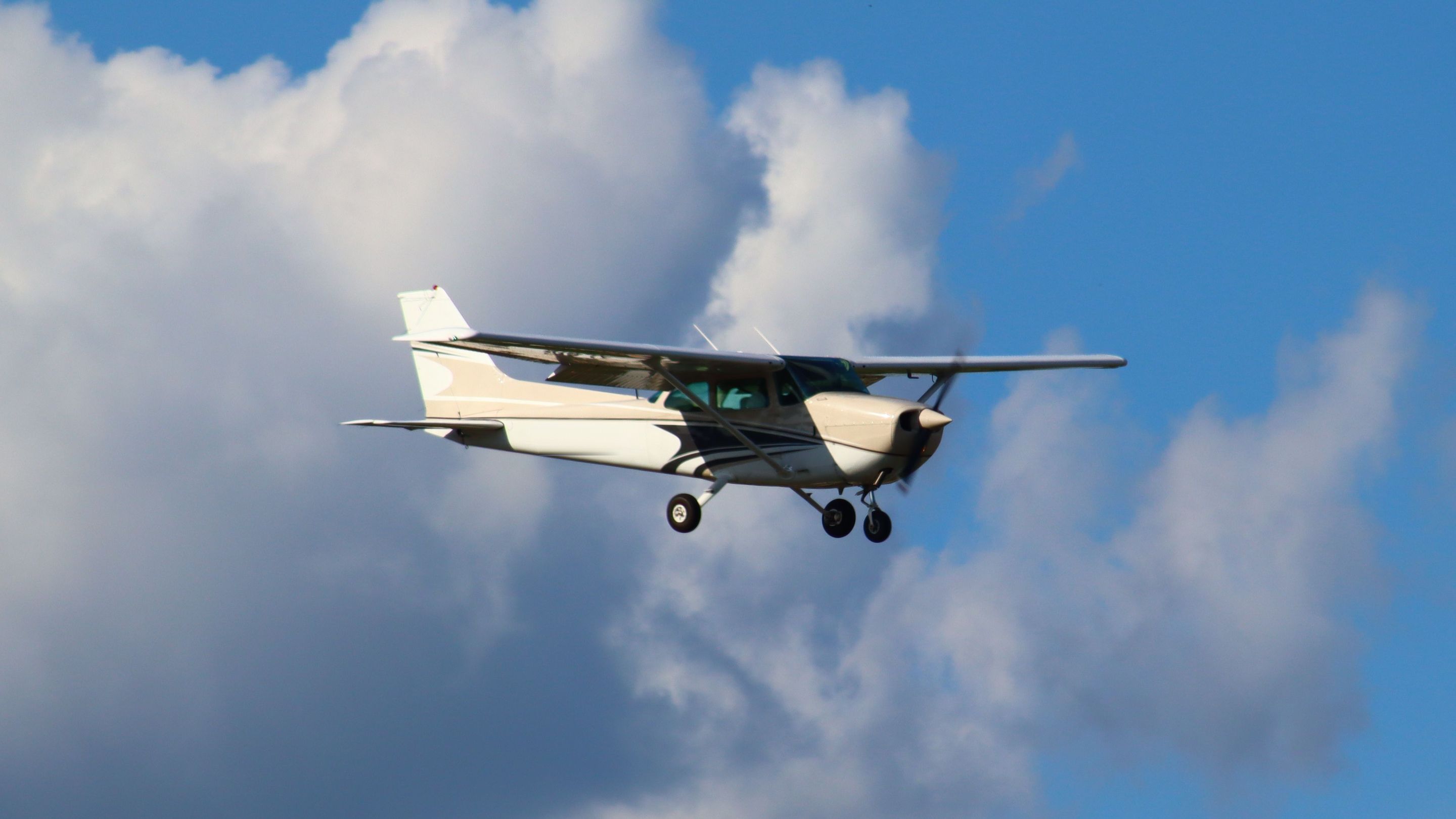 A Cessna 172 in flight against clouds and blue sky.