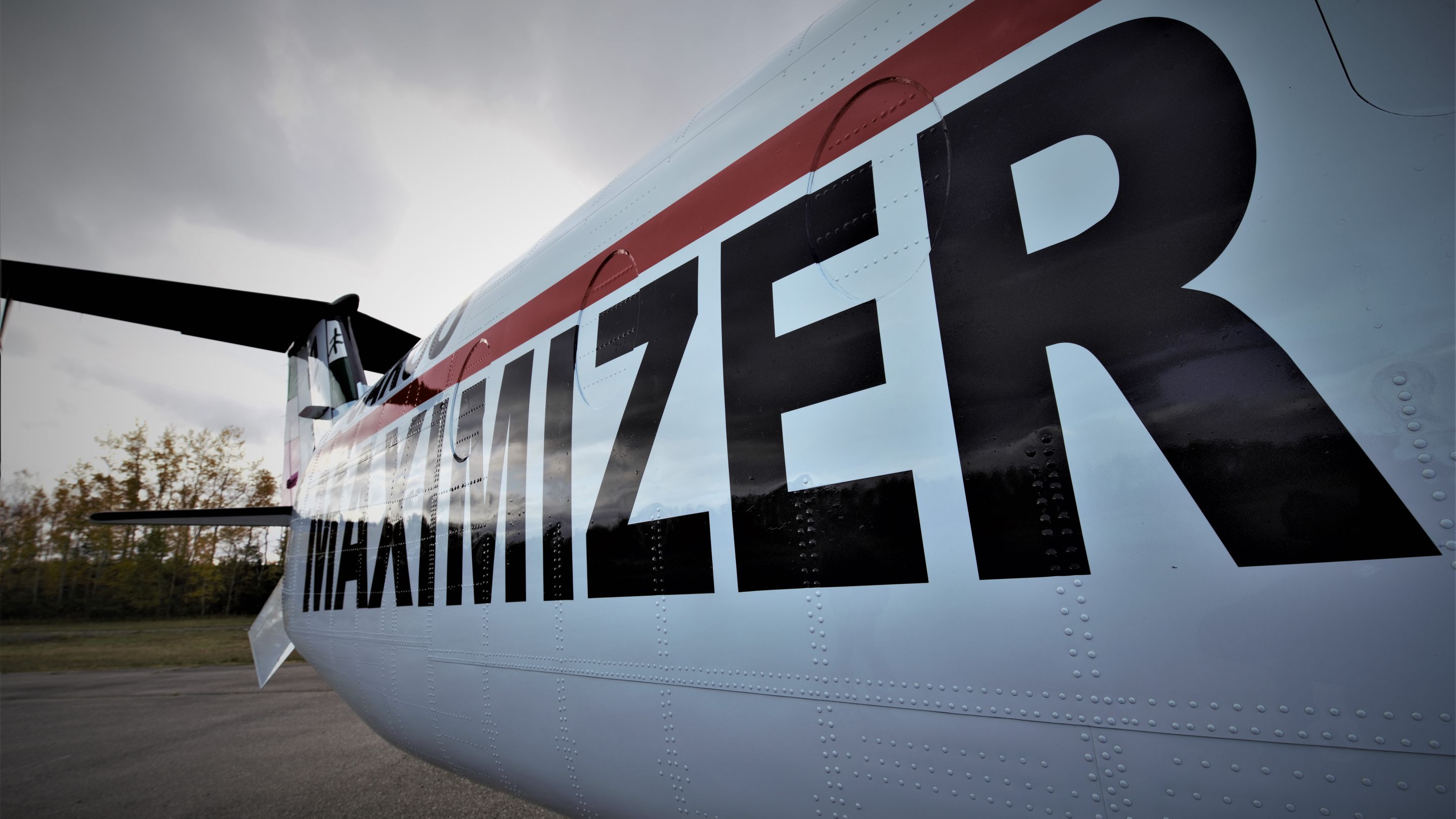 The fuselage of a Cargo Maximizer Beechcraft 1900D with a red stripe and large black lettering, seen from low on the ramp.