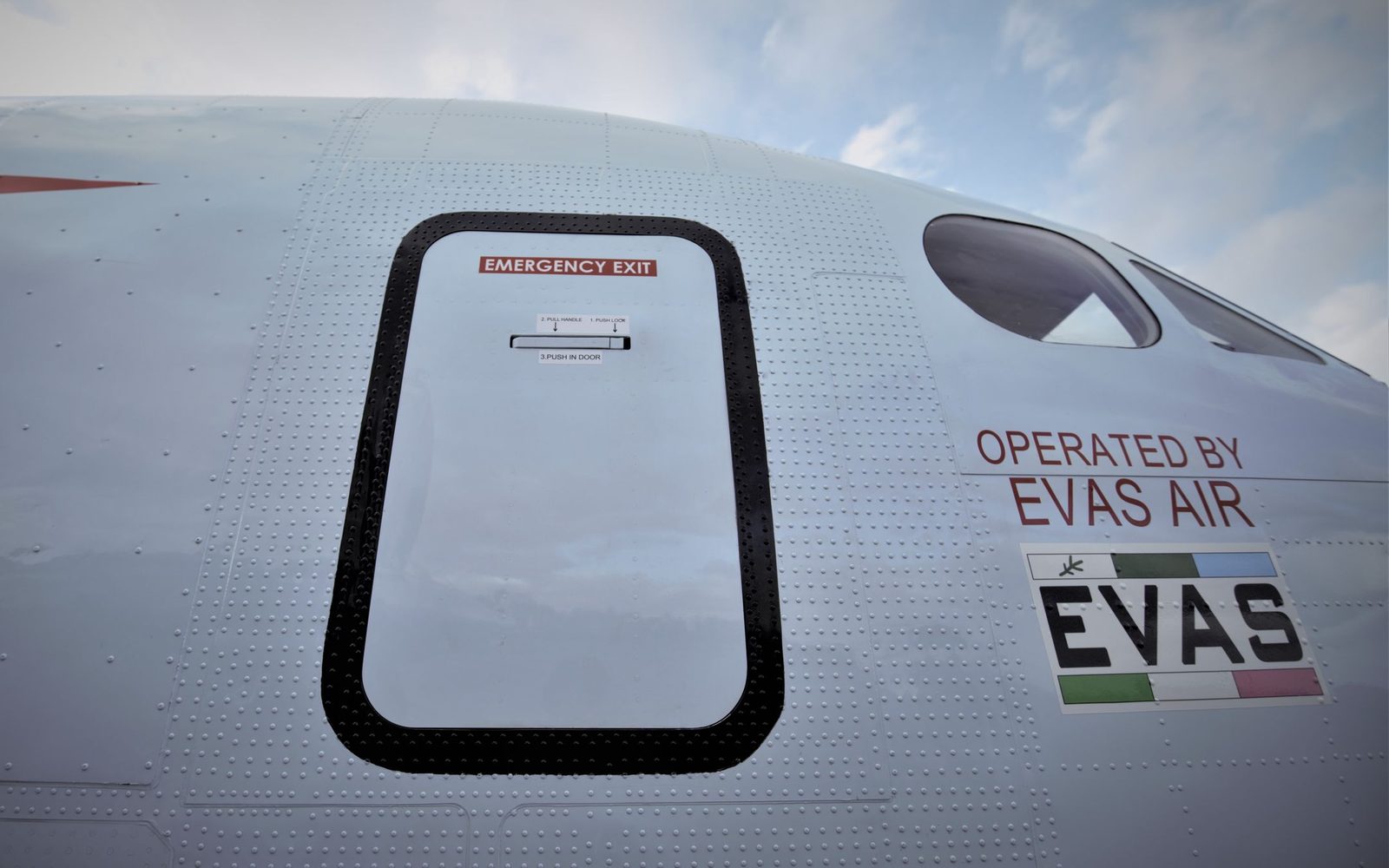 The emergency exit and Operated by EVAS Air marking on the fuselage of a Beechcraft 1900D